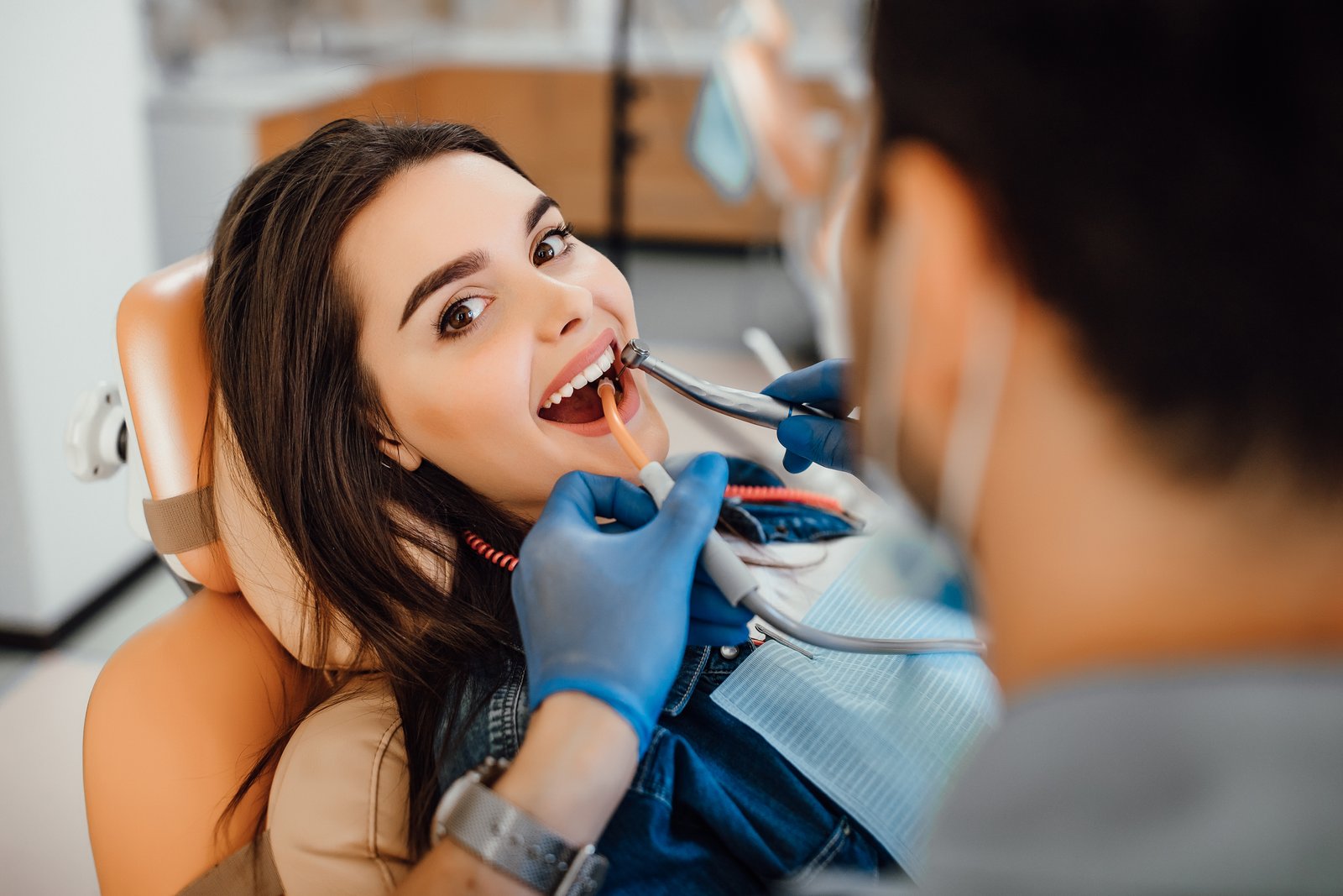 Smiling young woman in a dentist chair showcasing sparkling white teeth after a professional whitening treatment
